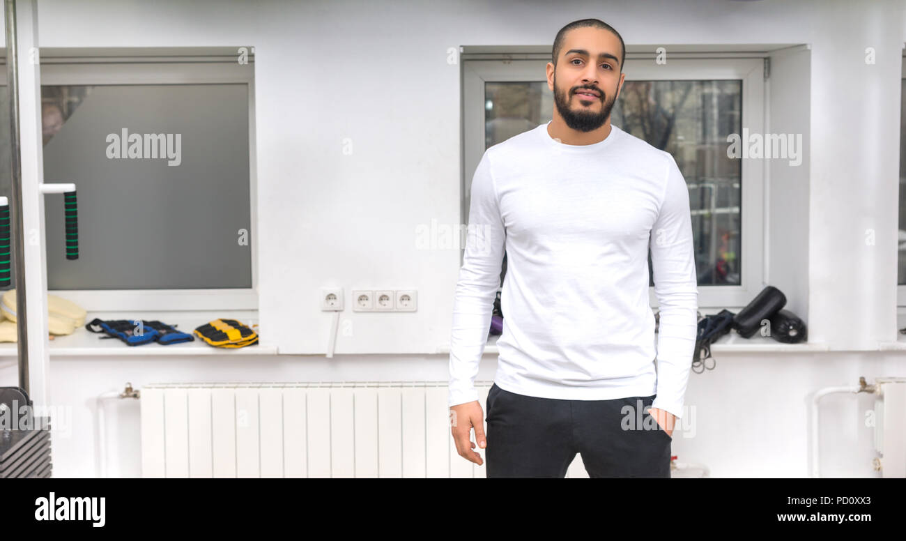 Entraîneur personnel sain monter dans un gymnase debout dans une position de détente avec sa main dans sa poche en souriant tranquillement à l'appareil photo Banque D'Images