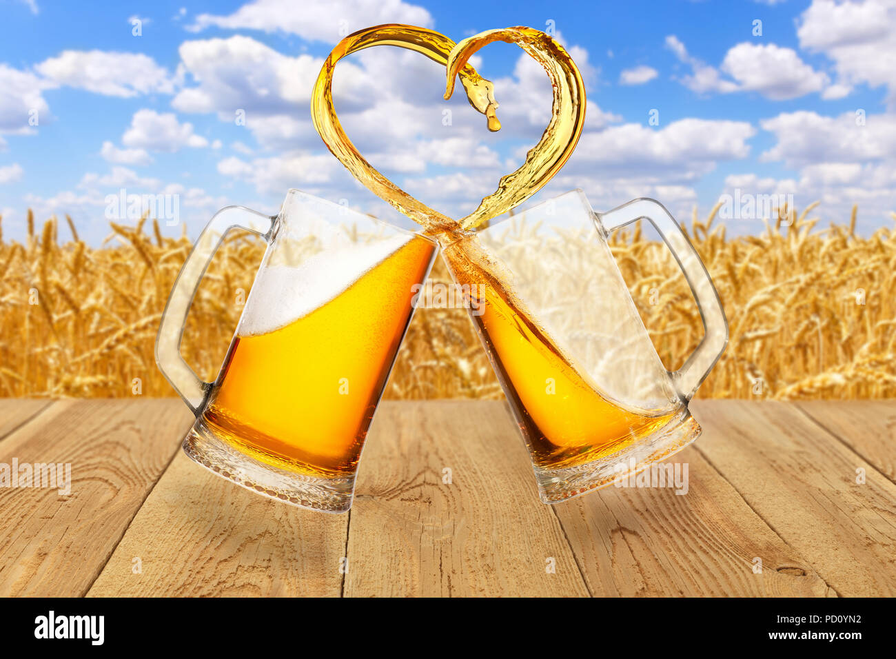 L'amour de la bière concept. Deux tasses en verre toasting et la création d'éclaboussure de forme de coeur sur fond de champ de blé mûr Banque D'Images