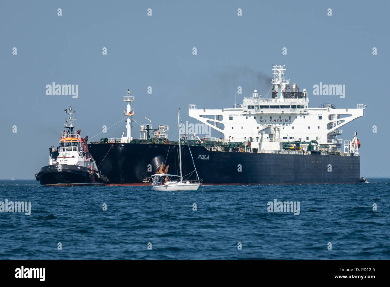 Trieste, Italie, le 4 août 2018. Un voilier se dépêche de sortir de la façon qu'un des guides de remorqueurs battant pavillon libérien Pola pétroliers dans la mer Adriatique p Banque D'Images