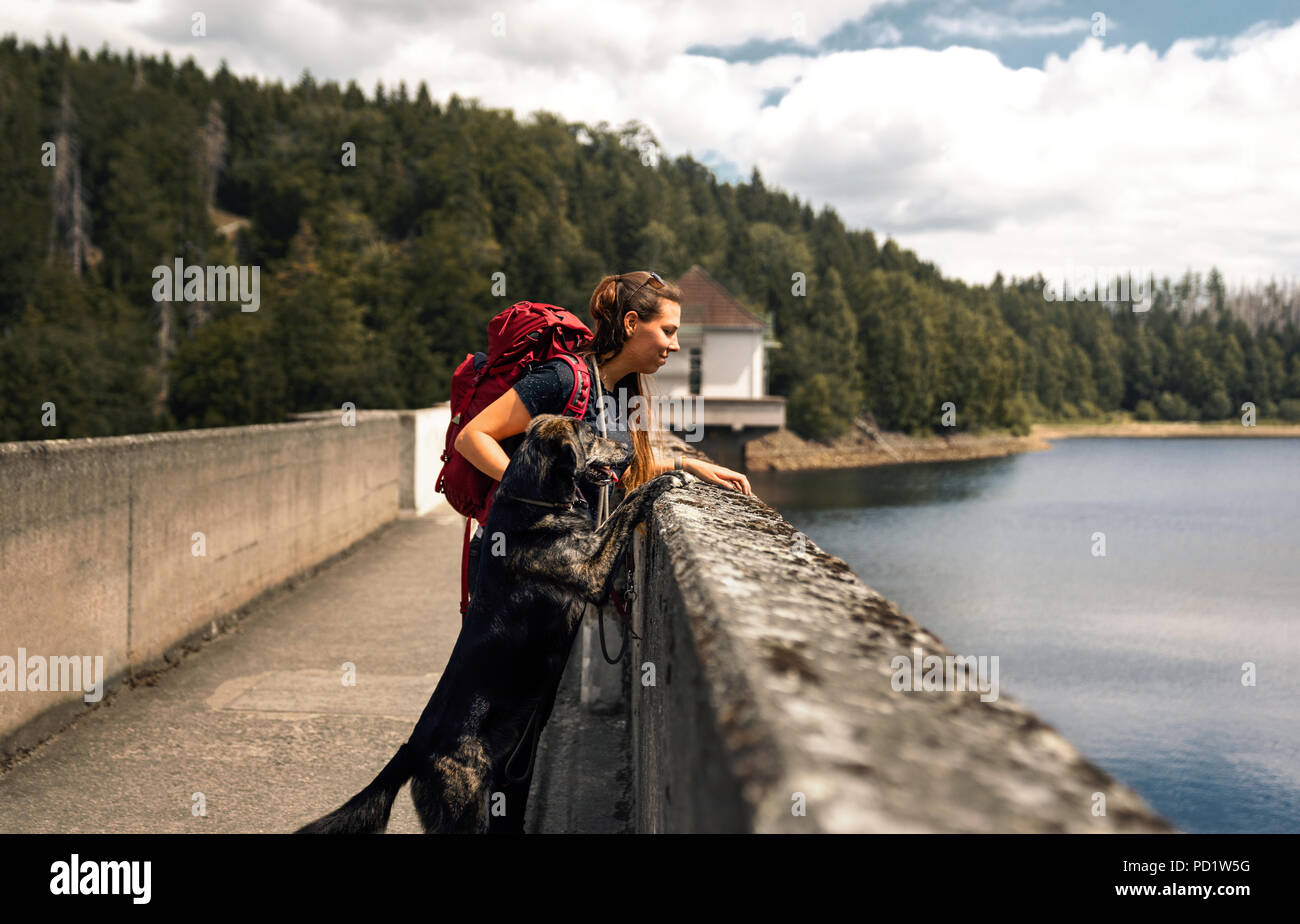 Jeune femme avec sac à dos et berger allemand chiot debout sur un pont en face de la forêt et lac Banque D'Images