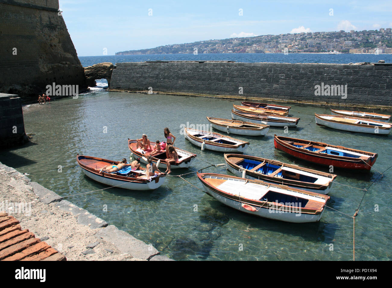 Les jeunes femmes et les enfants à prendre le soleil sur la location de chaloupes dans une petite baie protégée du vent à côté du Castel dell'Ovo en Naples, Italie Banque D'Images