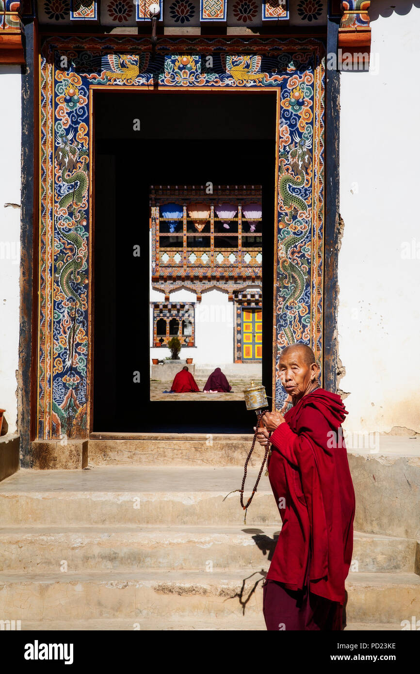 Un moine passe devant l'entrée de l'Kenchosum Lhakhang (monastère) dans la région de Jakar tout en travaillant son moulin à prières et des perles. Le District de Bumthang. Le Bhoutan. Banque D'Images