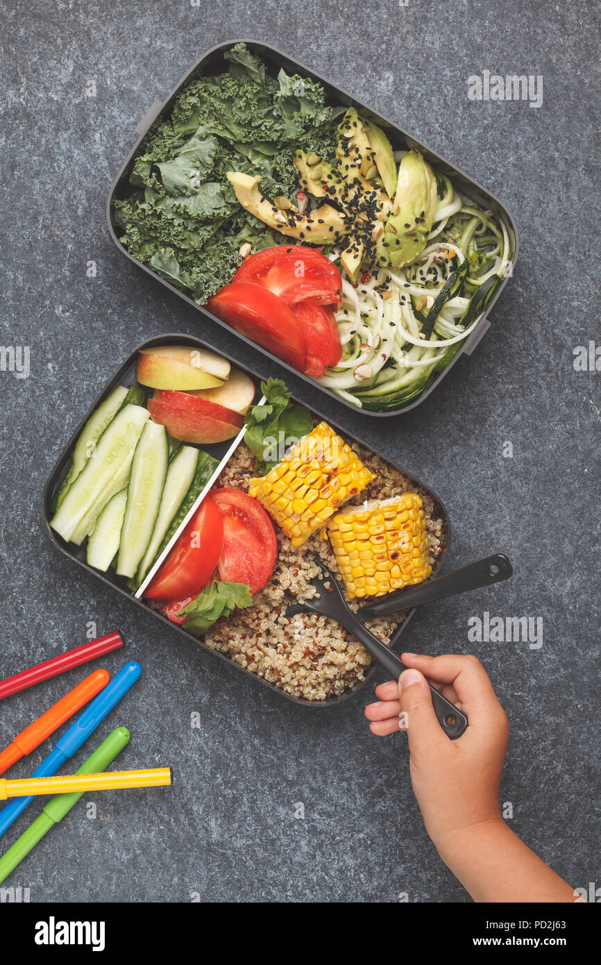 Préparation des repas sains avec des conteneurs le quinoa, l'avocat, le maïs, les courgettes nouilles et le chou frisé. La nourriture à emporter à l'école. Fond sombre, vue du dessus. Banque D'Images