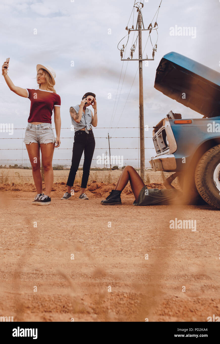 Femme faisant une vidéo selfies pour enregistrer la situation de voiture en panne, avec des amis d'essayer de résoudre le problème. Banque D'Images