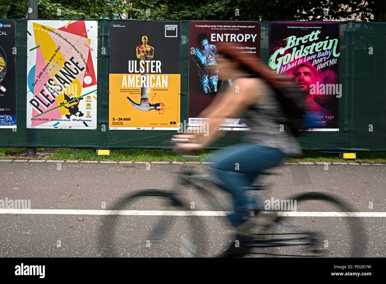 Un cycliste féminin rides par des affiches publicitaires pour Edinburgh Fringe Festival montre dans les prés, Édimbourg, Écosse, Royaume-Uni. Banque D'Images