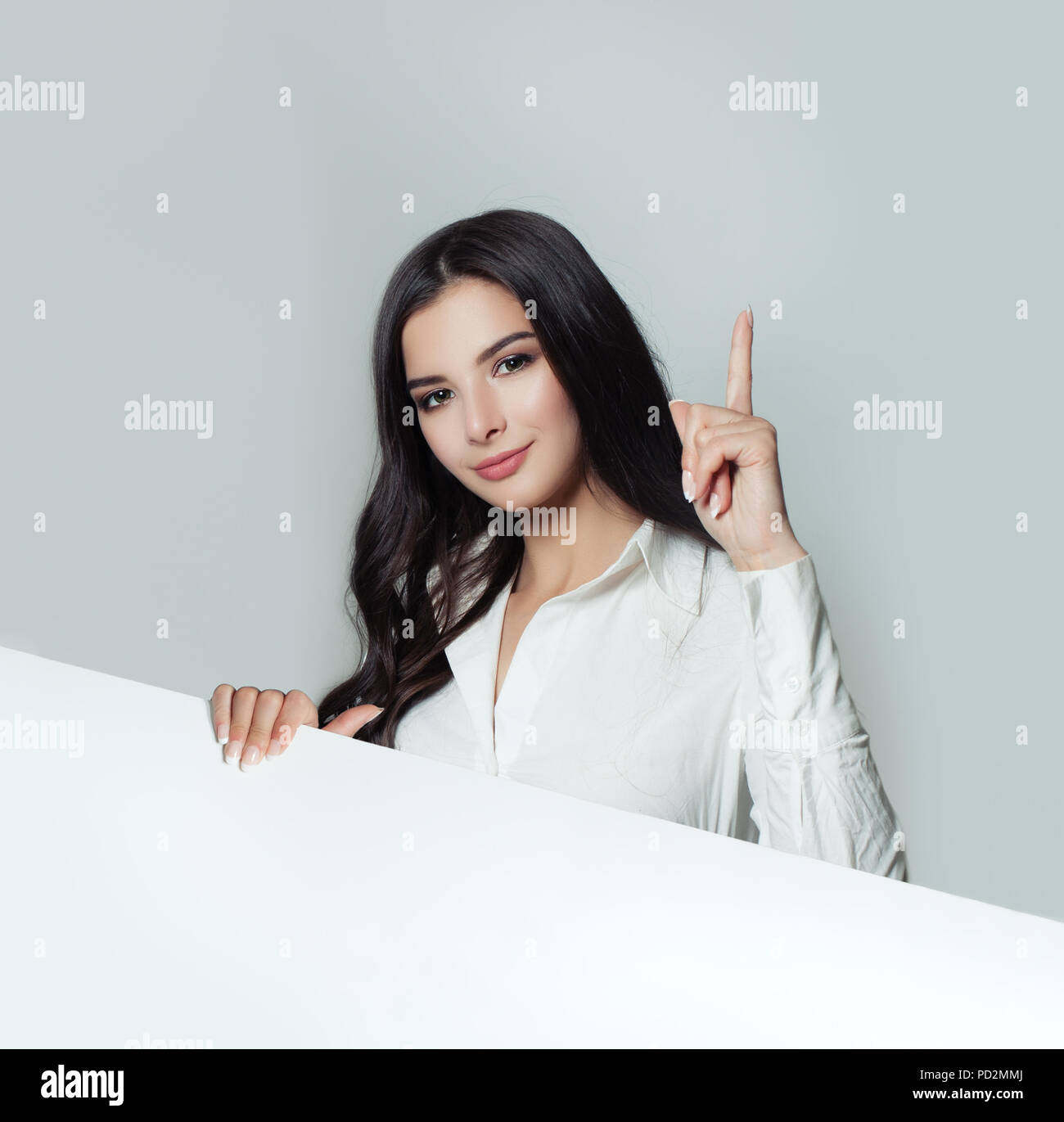 Cute business woman pointing up et holding paper board avec espace salon exemplaire vierge pour slogan, advertisiment ou message texte sur fond blanc. Suc Banque D'Images