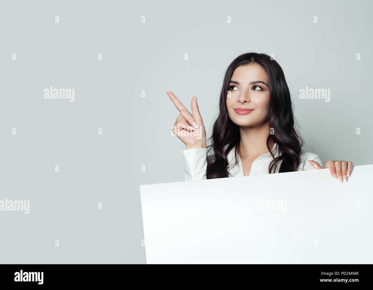 Happy young businesswoman pointing up et montrant pancarte avec espace salon exemplaire vierge pour slogan, advertisiment ou message texte sur fond blanc. Banque D'Images