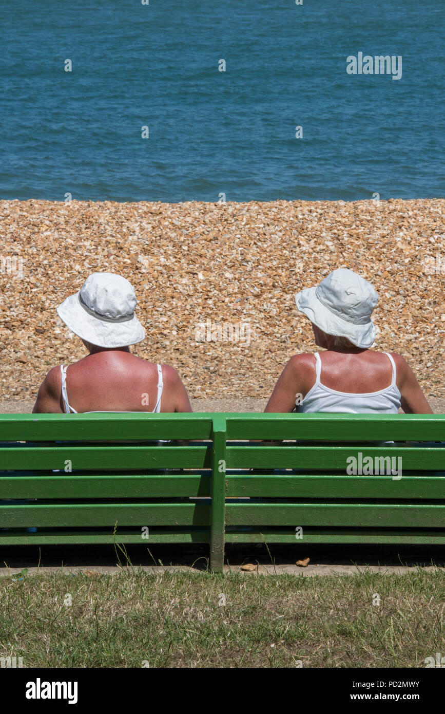 Remorquer des dames plus âgées ou des amis assis sur un banc en bois peint en vert portant des chapeaux de soleil dans la vague de fortes chaleurs en été. la retraite au soleil. Banque D'Images