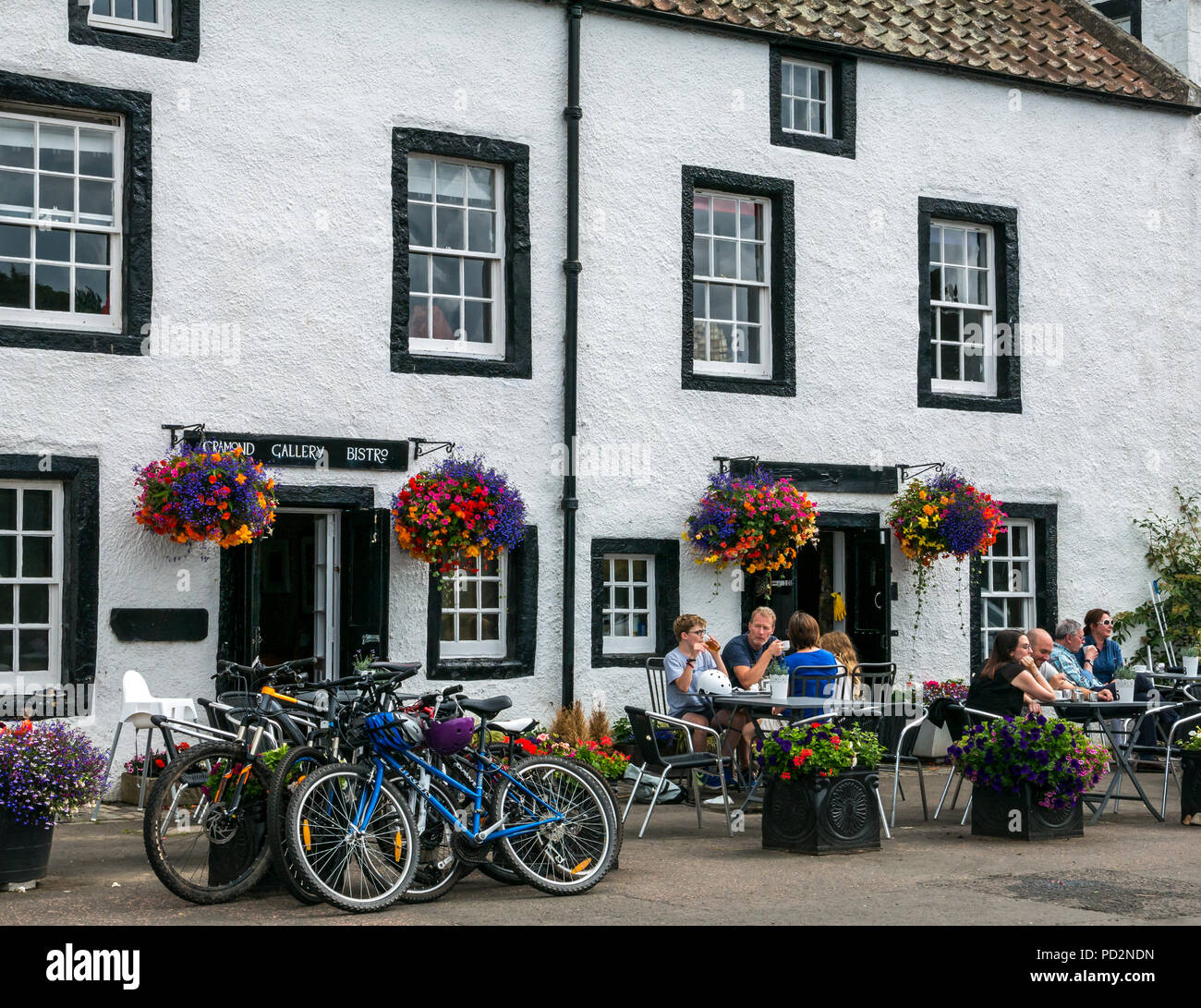 Les gens assis à des tables avec des vélos garés, Cramond Gallery Bistro, Cramond, Edinburgh, Scotland, UK avec des paniers de fleurs en été Banque D'Images