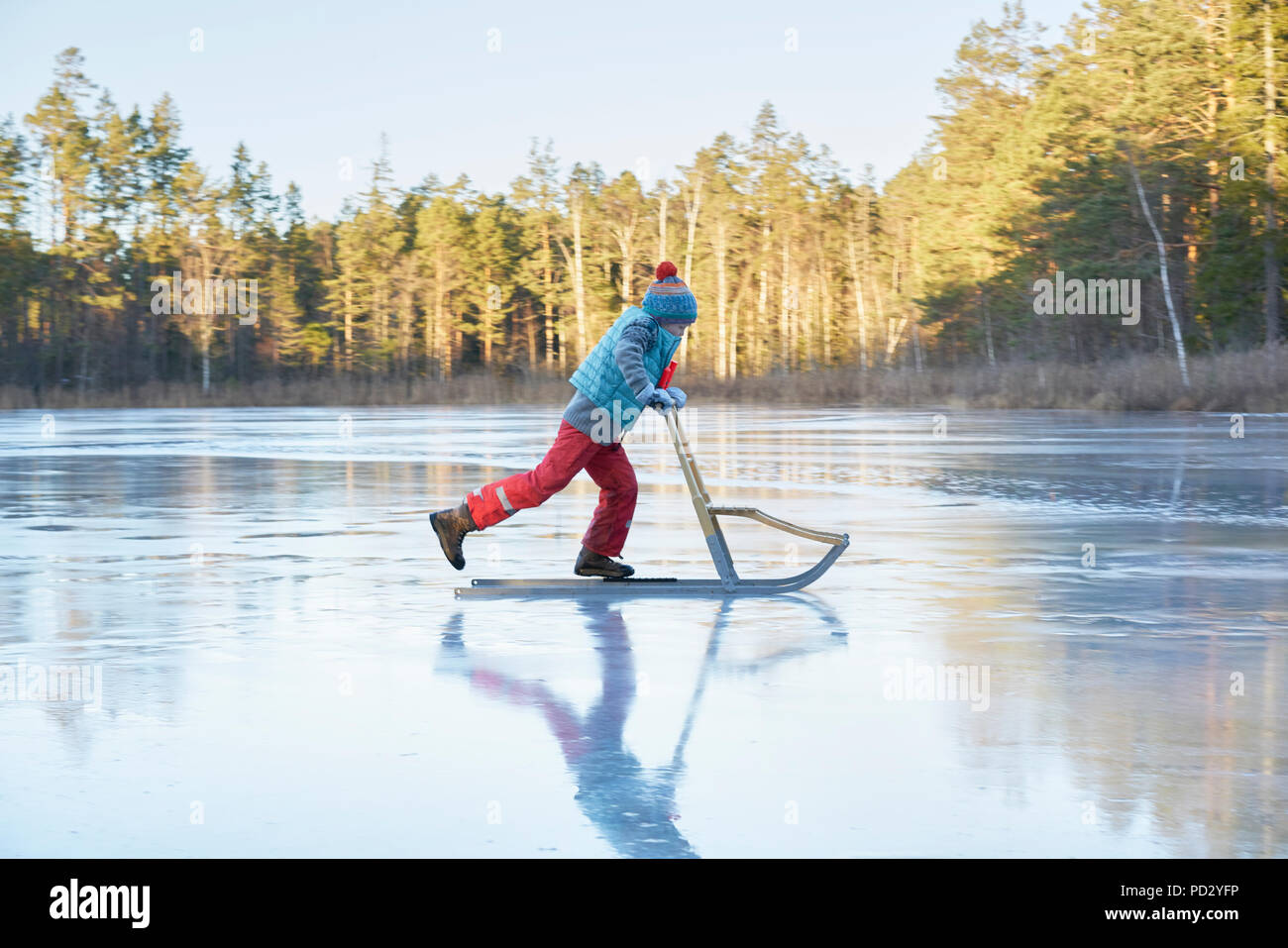 Garçon patinage sur le lac gelé en traîneau Banque D'Images