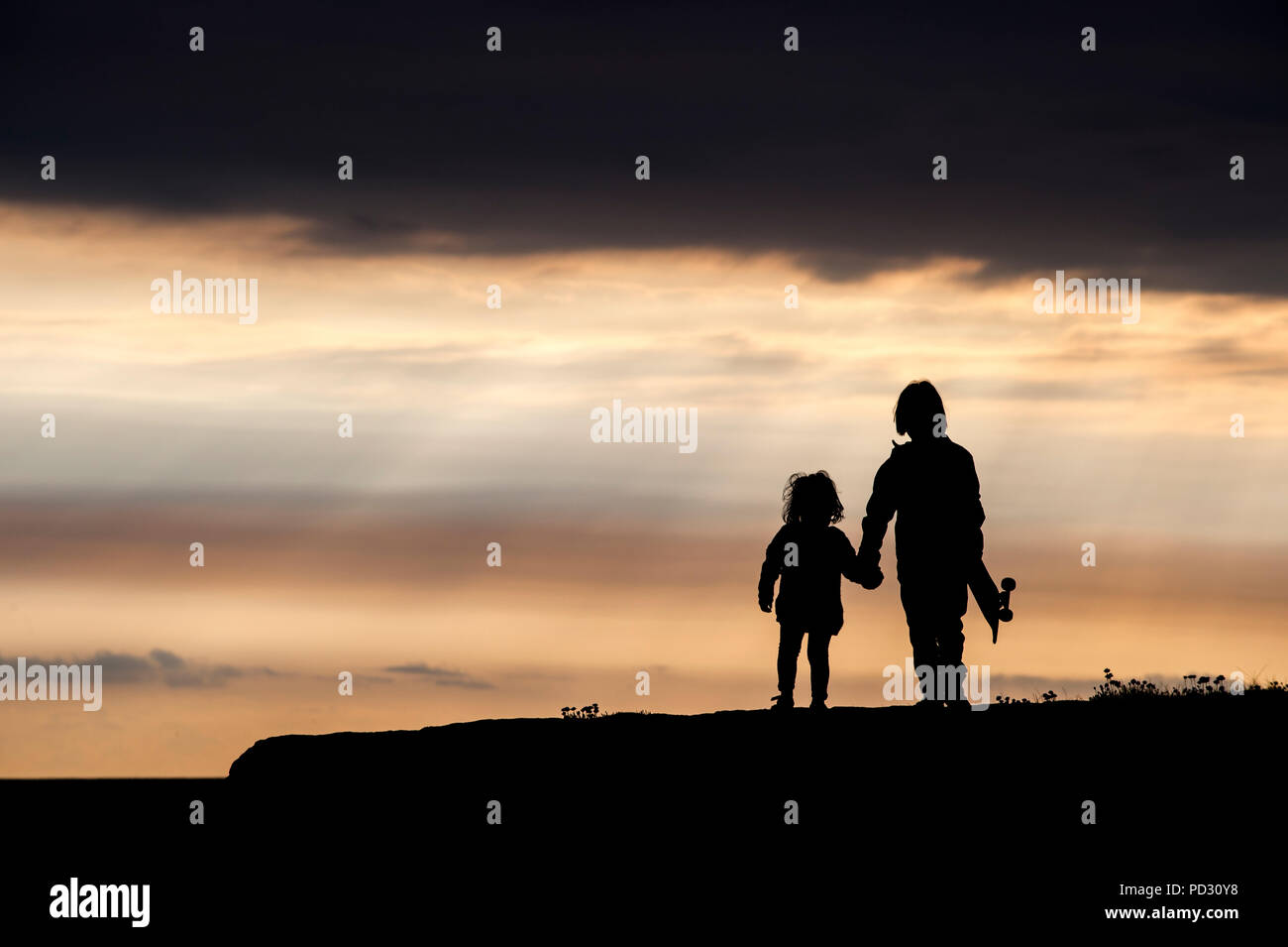 Frère et sœur, marche main dans la main, au coucher du soleil, Doolin, Clare, Irlande Banque D'Images