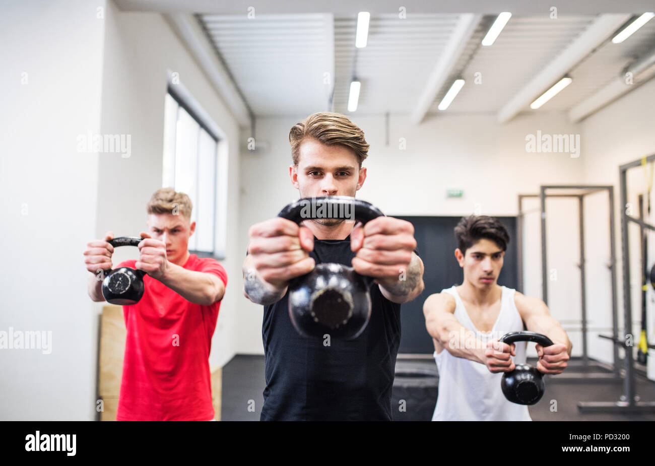 Trois jeunes hommes dans la salle de gym faire kettlebell swings. Banque D'Images