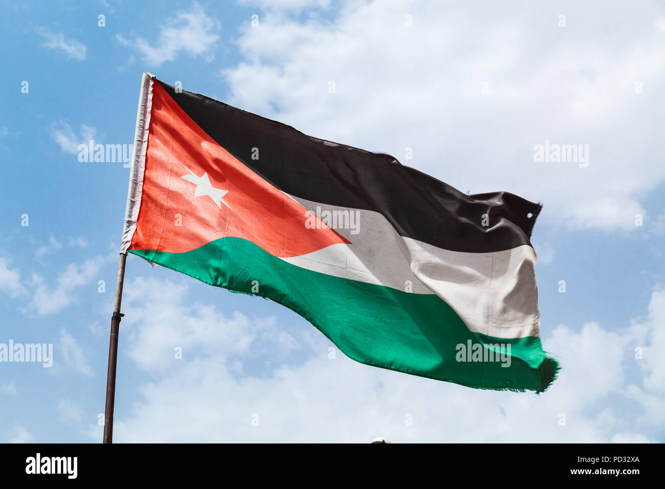 Brandissant le drapeau de la Jordanie sur le vent sur ciel nuageux Banque D'Images