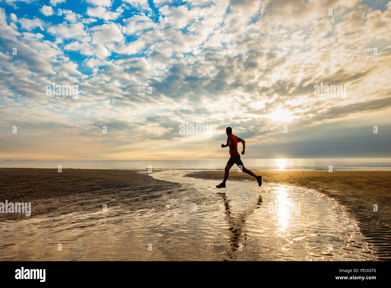 Homme mature, 50-60 ans, jogging, course sur la plage au lever du soleil. ROYAUME-UNI Banque D'Images
