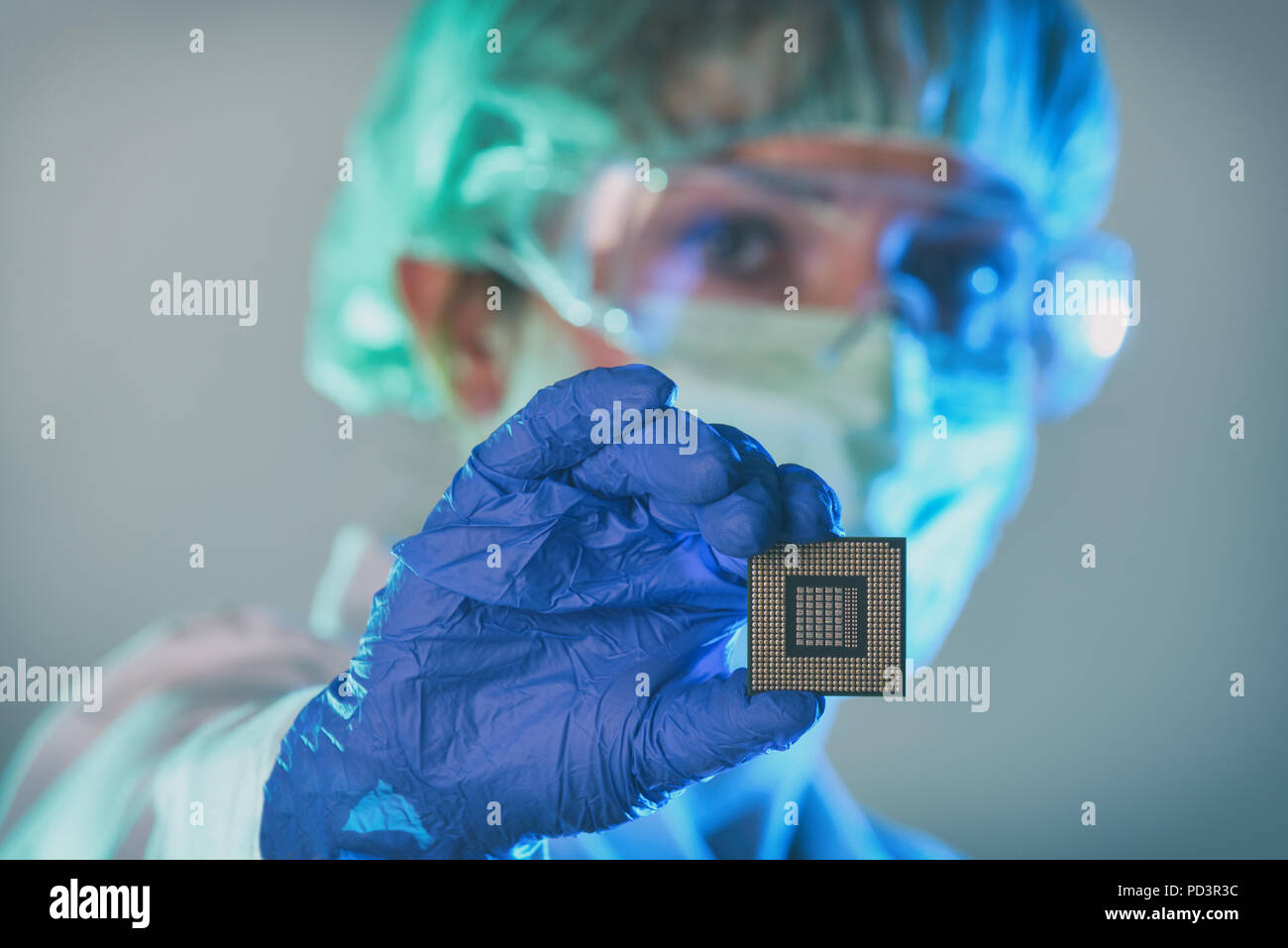 Un ingénieur travaillant dans un laboratoire portant un uniforme spécial et de gants est titulaire nouveau processeur dans les mains et l'examine Banque D'Images