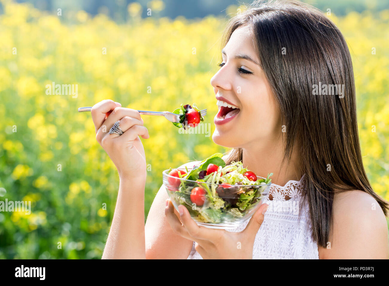 Face Close up shot of attractive girl eating salad sain en plein air avec champ de fleur en arrière-plan. Banque D'Images