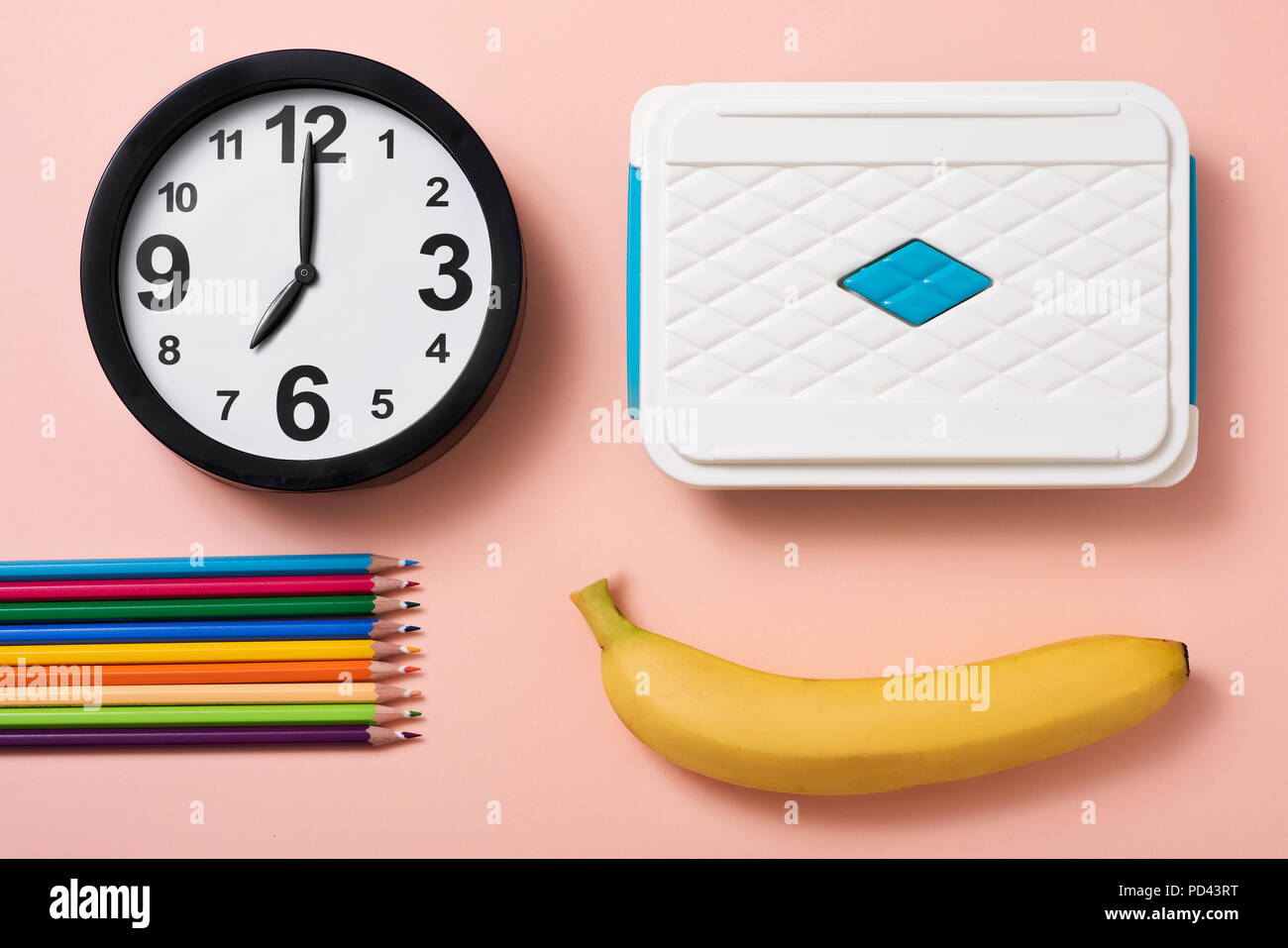 Portrait d'un réveil à sept heures, certains des crayons de couleurs différentes, une banane et un lunch box sur un fond rose saumon Banque D'Images