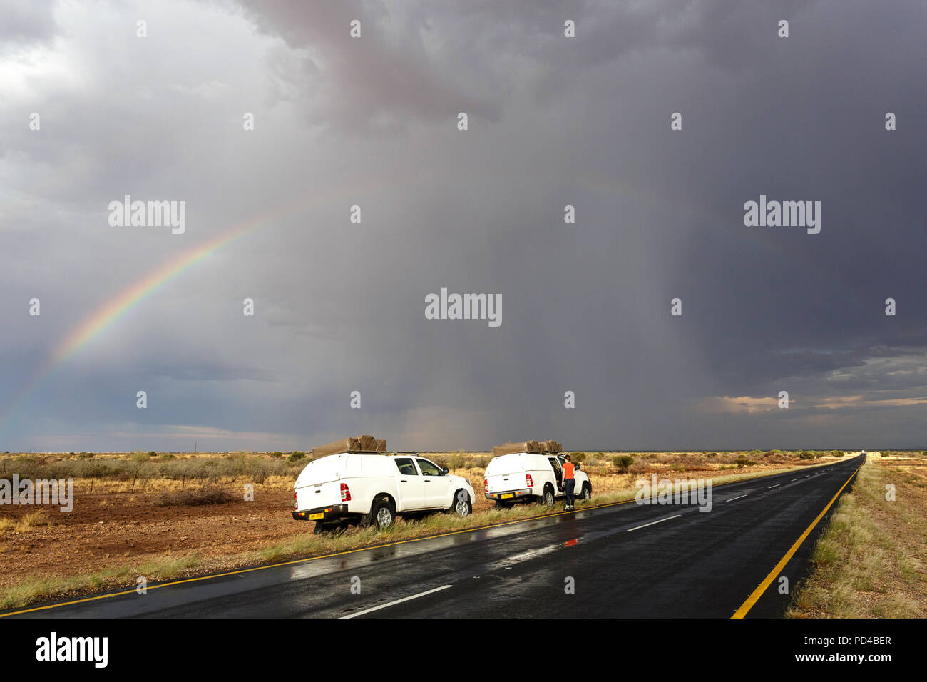 Voitures de tourisme 4x4 garé par route pavée dans stormy weather conditions avec un arc-en-ciel sur la route, la Namibie Banque D'Images