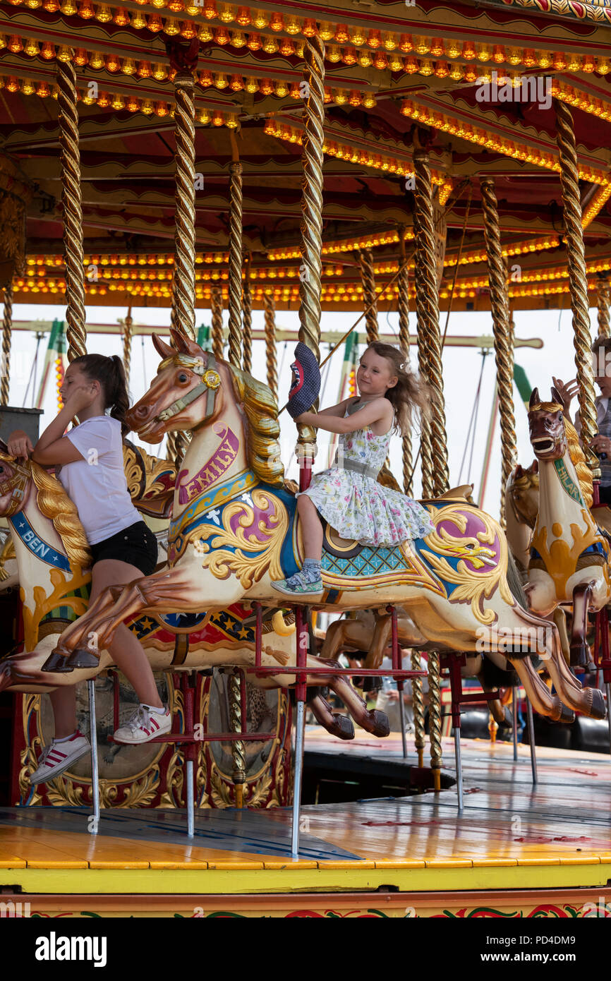 Enfants sur un cheval au galop à vapeur carrousel, fairground ride à un bain à vapeur juste. L'Angleterre Banque D'Images