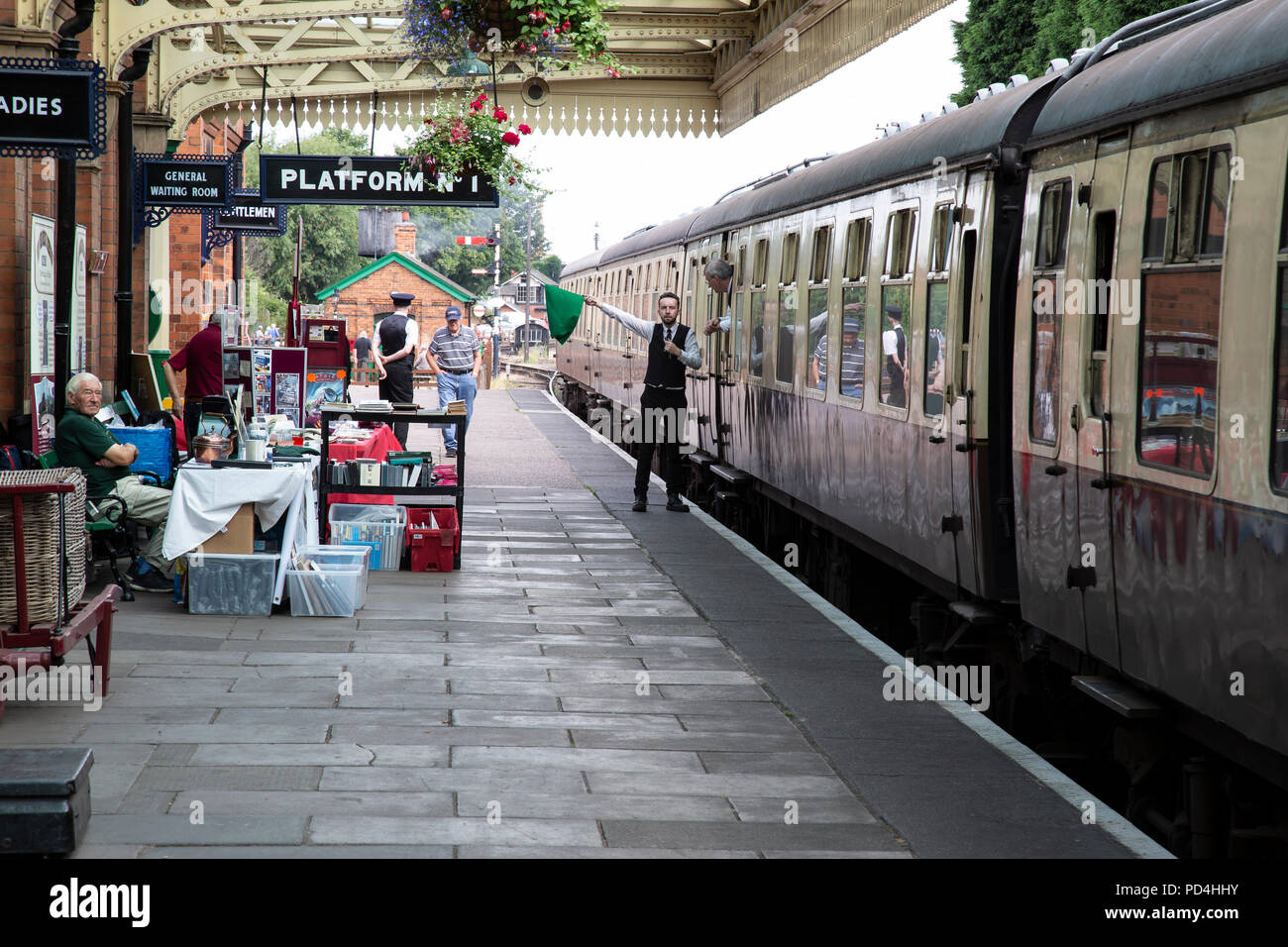 Garde de fer sur le Great Central Railway heritage line qui agitait un drapeau vert pour signaler 'tout de suite' pour le pilote du moteur à Loughborough gare Banque D'Images