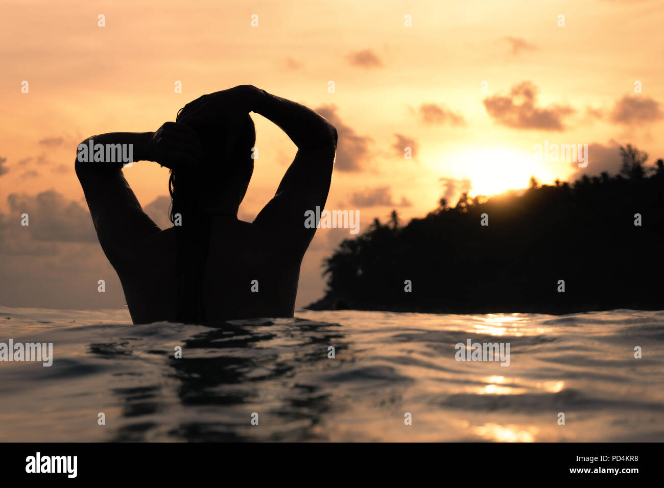Jeune femme par derrière dans le bain de l'océan indien et en maintenant ses cheveux pendant le coucher du soleil violet with copy space Banque D'Images