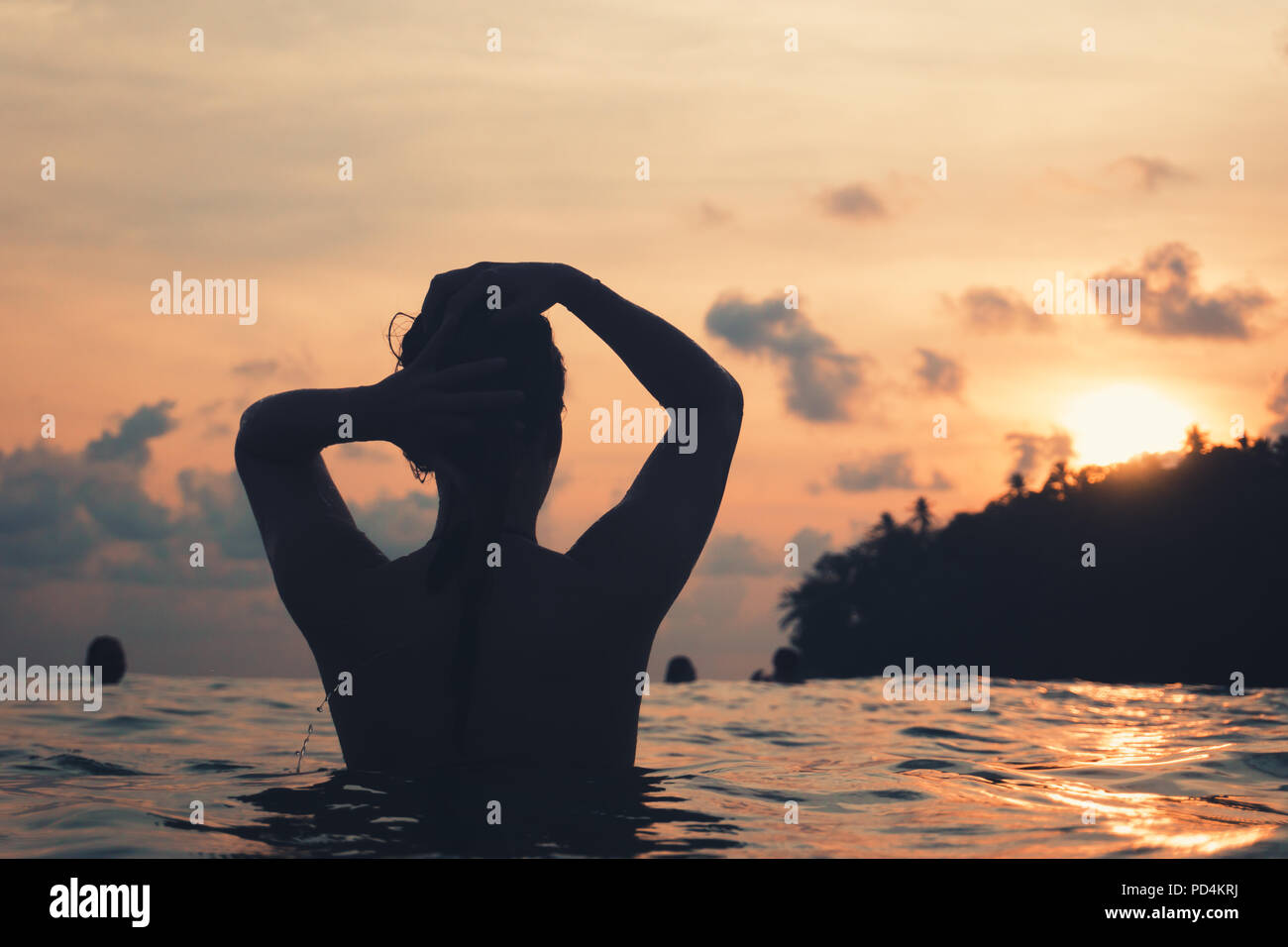 Jeune femme par derrière dans le bain de l'océan indien et en maintenant ses cheveux pendant le coucher du soleil violet with copy space Banque D'Images