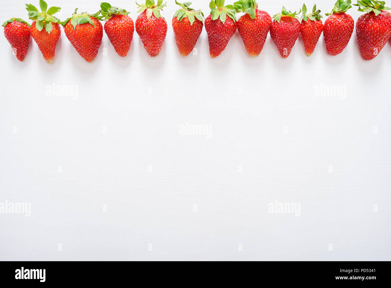 Les fraises dans une rangée sur la table en bois blanc arrière-plan. Banque D'Images