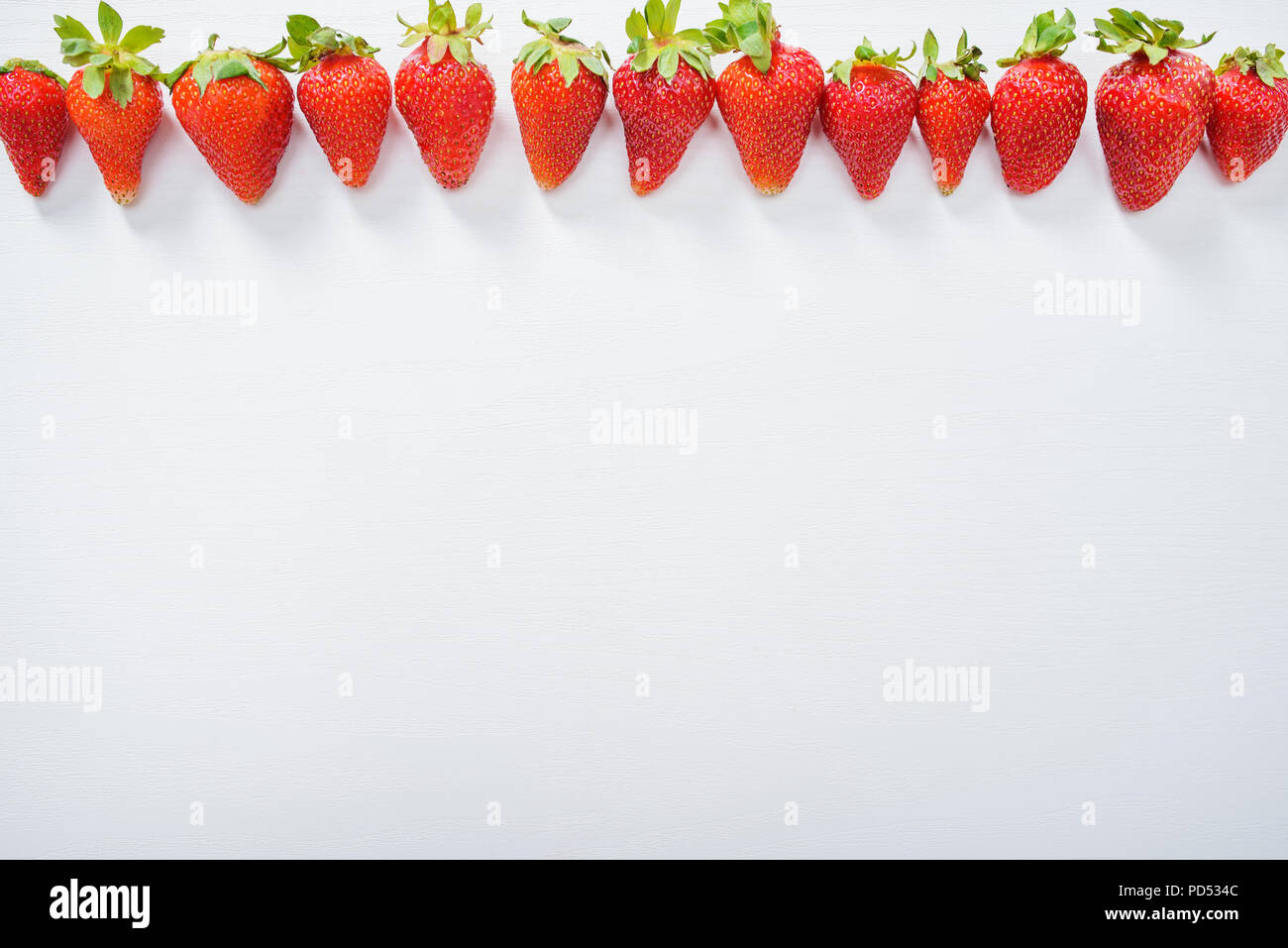 Les fraises dans une rangée sur la table en bois blanc arrière-plan. Banque D'Images
