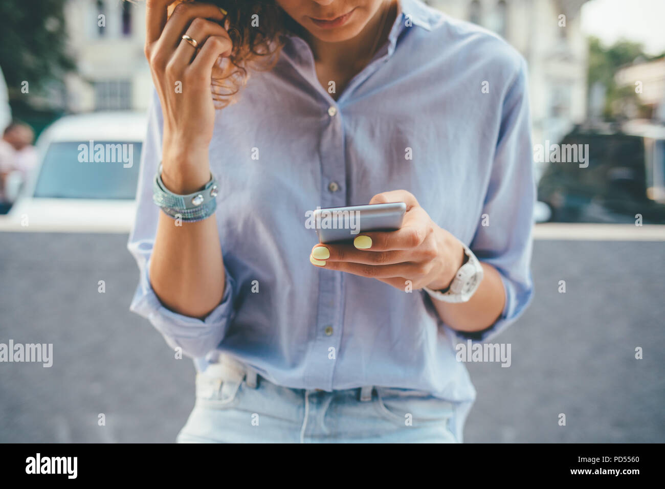 Jeune femme portant un t-shirt bleu et un jean à l'aide d'appareil mobile en ville. Close-up de la main de femme avec manucure jaune holding smart phone sur l'extérieur Banque D'Images
