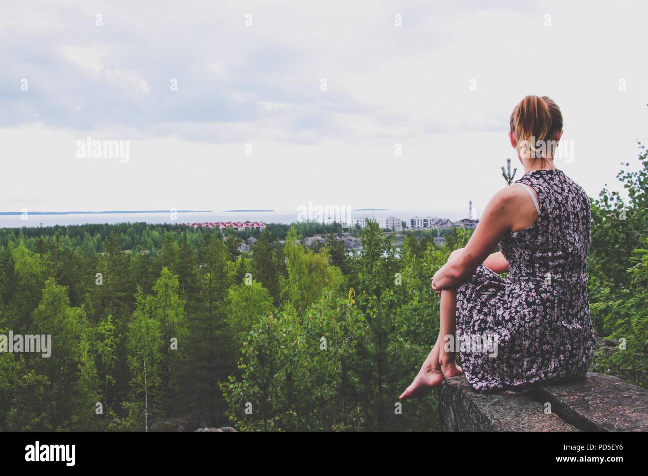 Une jeune fille dans une robe se situe sur une saillie rocheuse au-dessus de la forêt, qui est situé sur le bord d'un immense lac. À partir de la hauteur vous pouvez voir les chambres spacieuses Banque D'Images