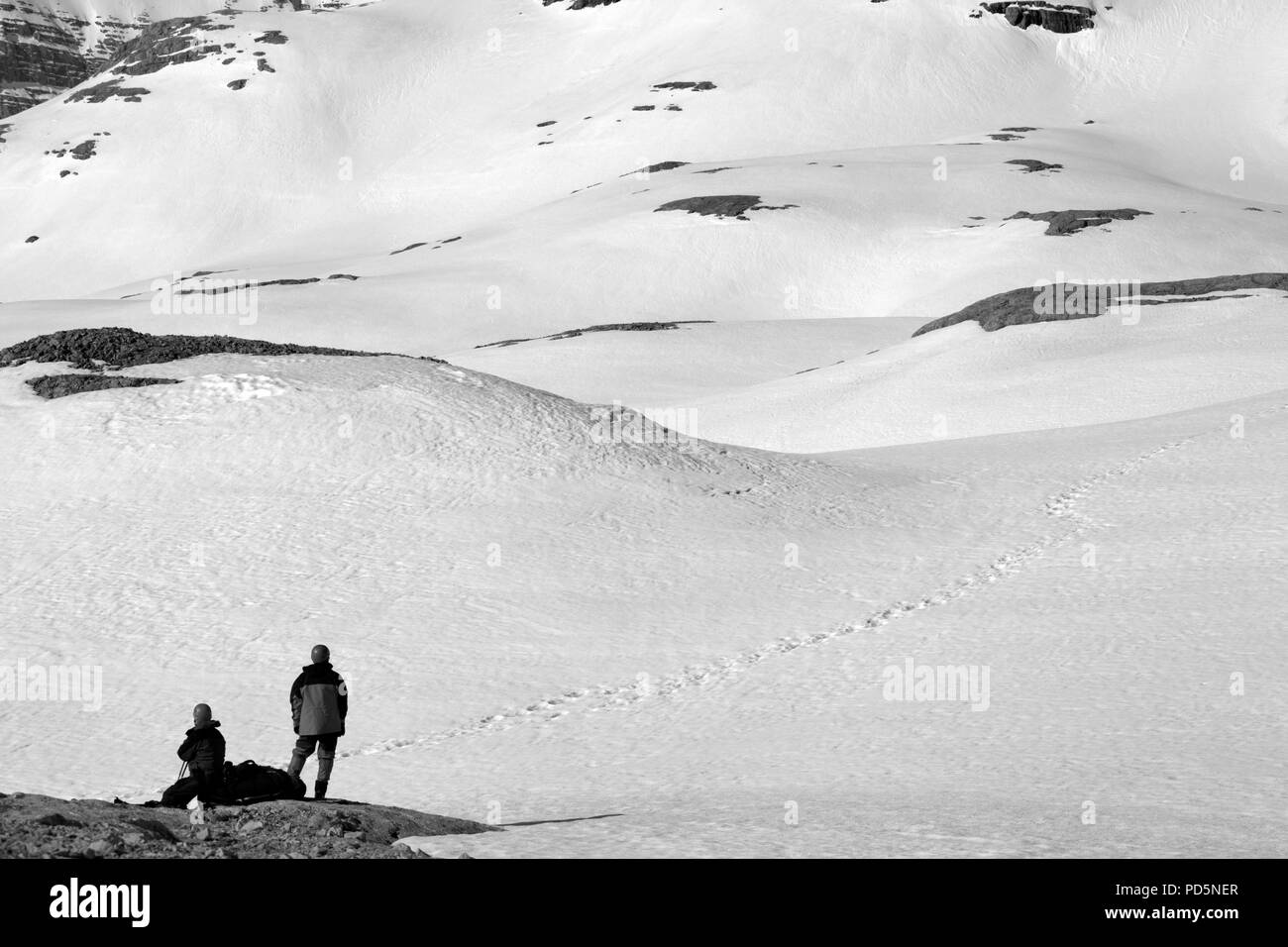 Deux randonneurs sur halte dans la montagne enneigée. Paysage aux tons noir et blanc. Banque D'Images