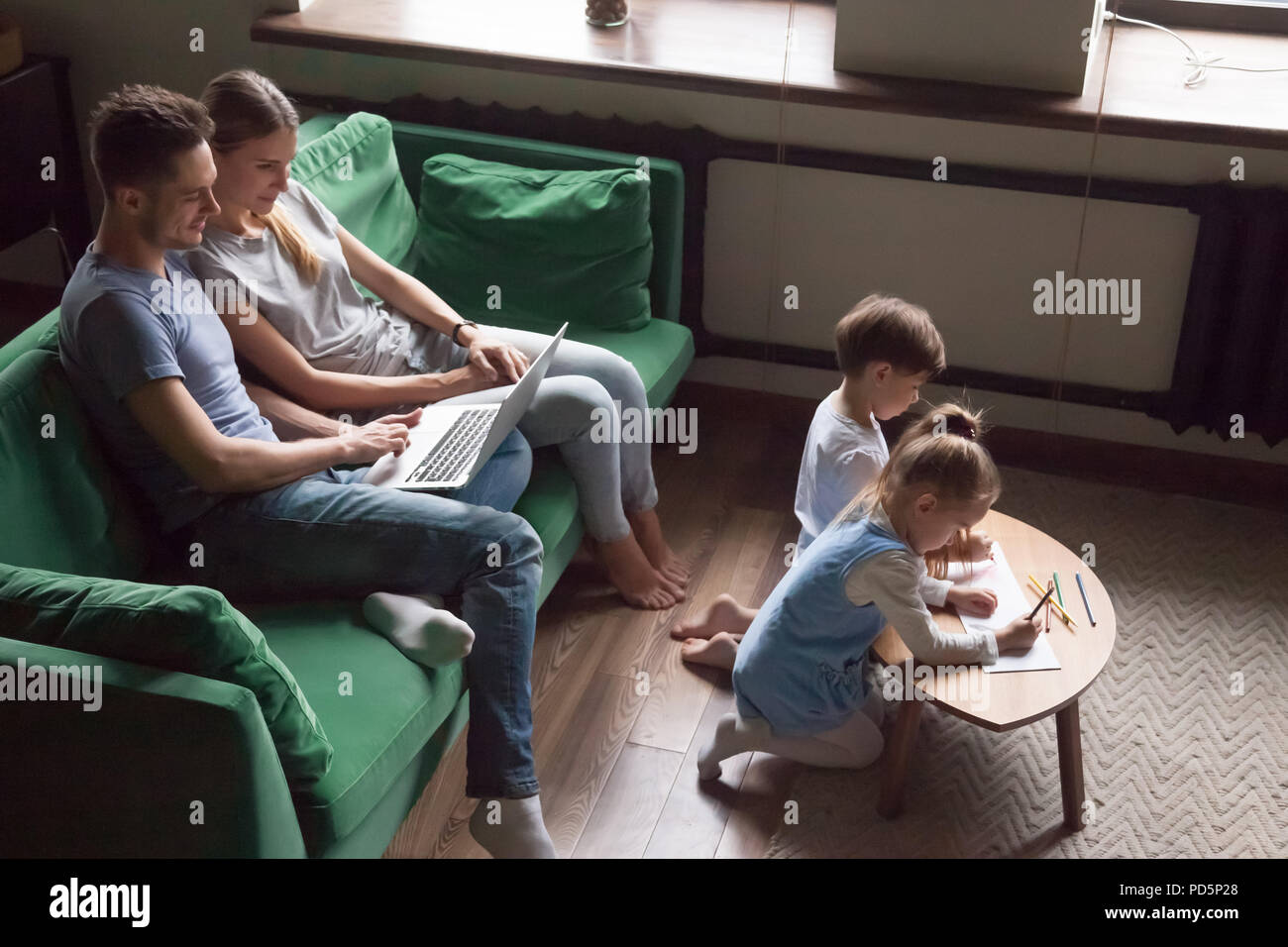 Les enfants de mêmes parents dimensions ensemble pendant que les parents à l'aide d'ordinateur portable à la CDM Banque D'Images