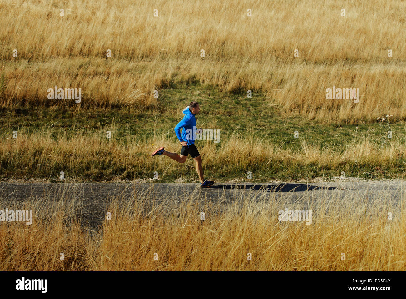 Coureur mâle s'exécutant sur route asphaltée en veste bleue et collants noirs Banque D'Images