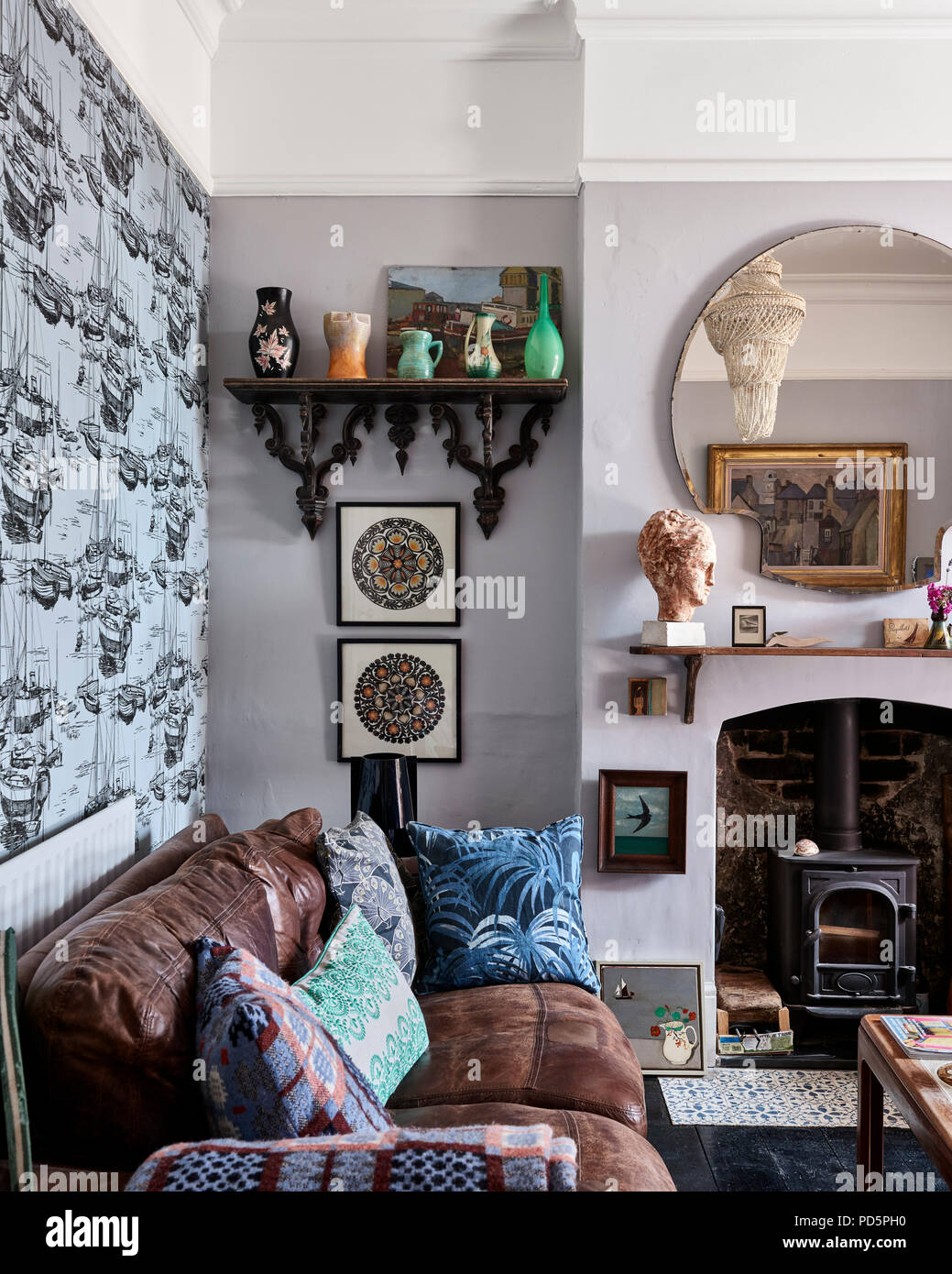 Dans Ceulean Zingara wallpaper par mer peu Greene dans petit salon avec canapé en cuir et poêle à bois. Le palm imprimer coussin est par Chambre des Banque D'Images