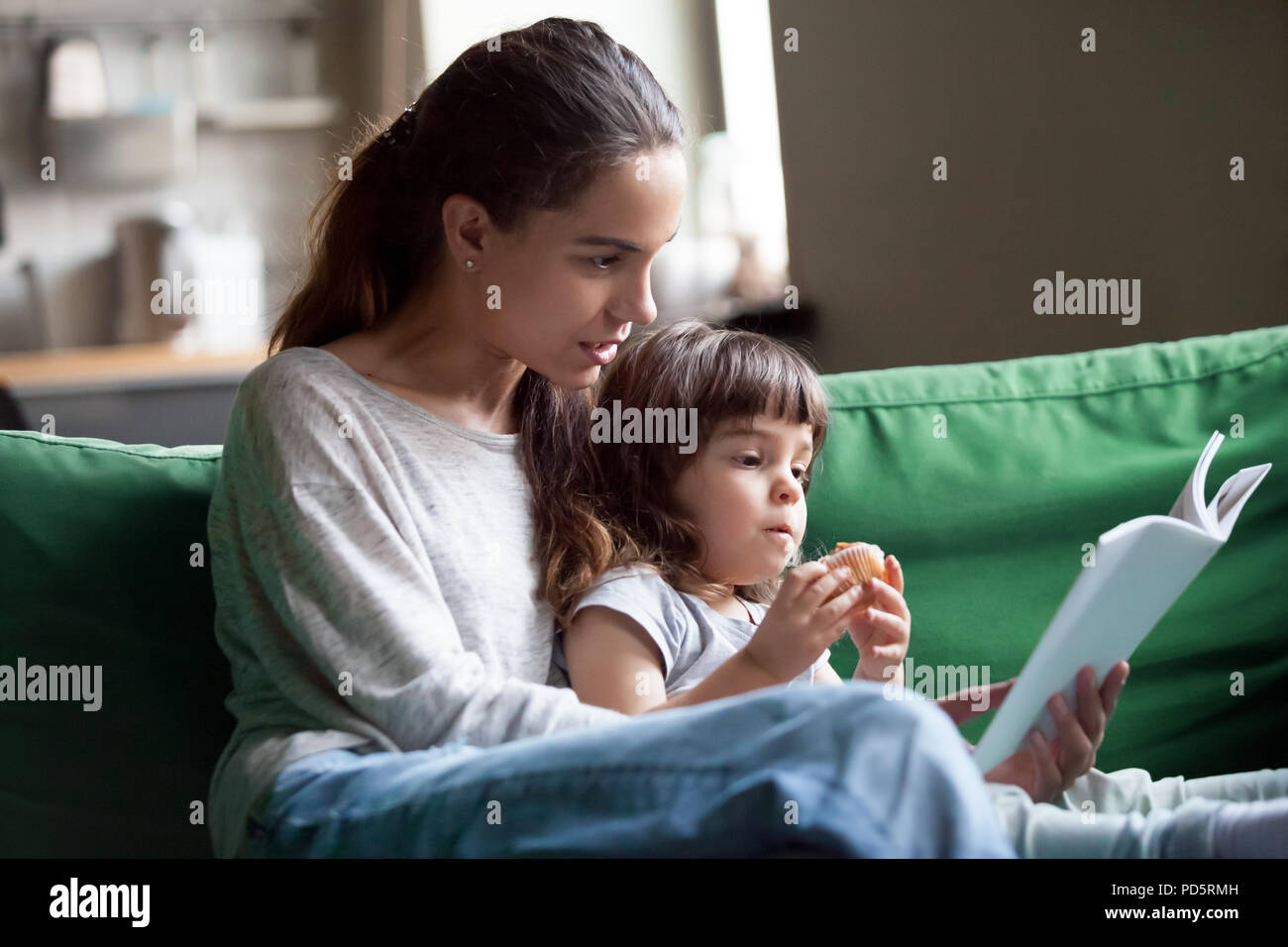 Mother and Daughter reading book sitting on sofa at home Banque D'Images