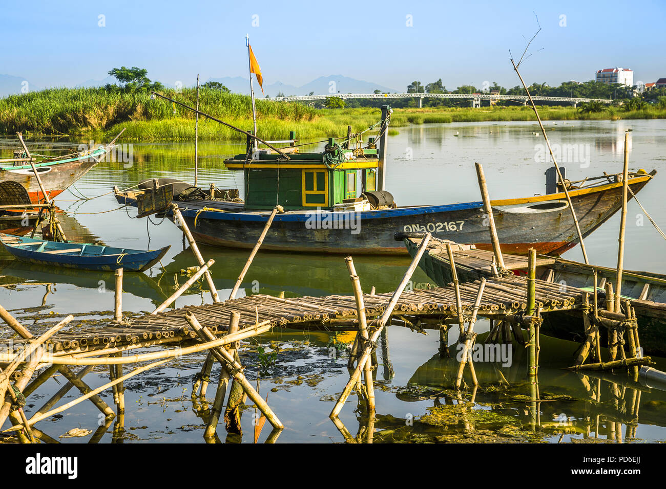 Un bateau de pêche derrière un bamboo dock et à l'avant de la chaîne à la rivière de cam Kim de l'autre côté de la baie de Hoi An. Banque D'Images