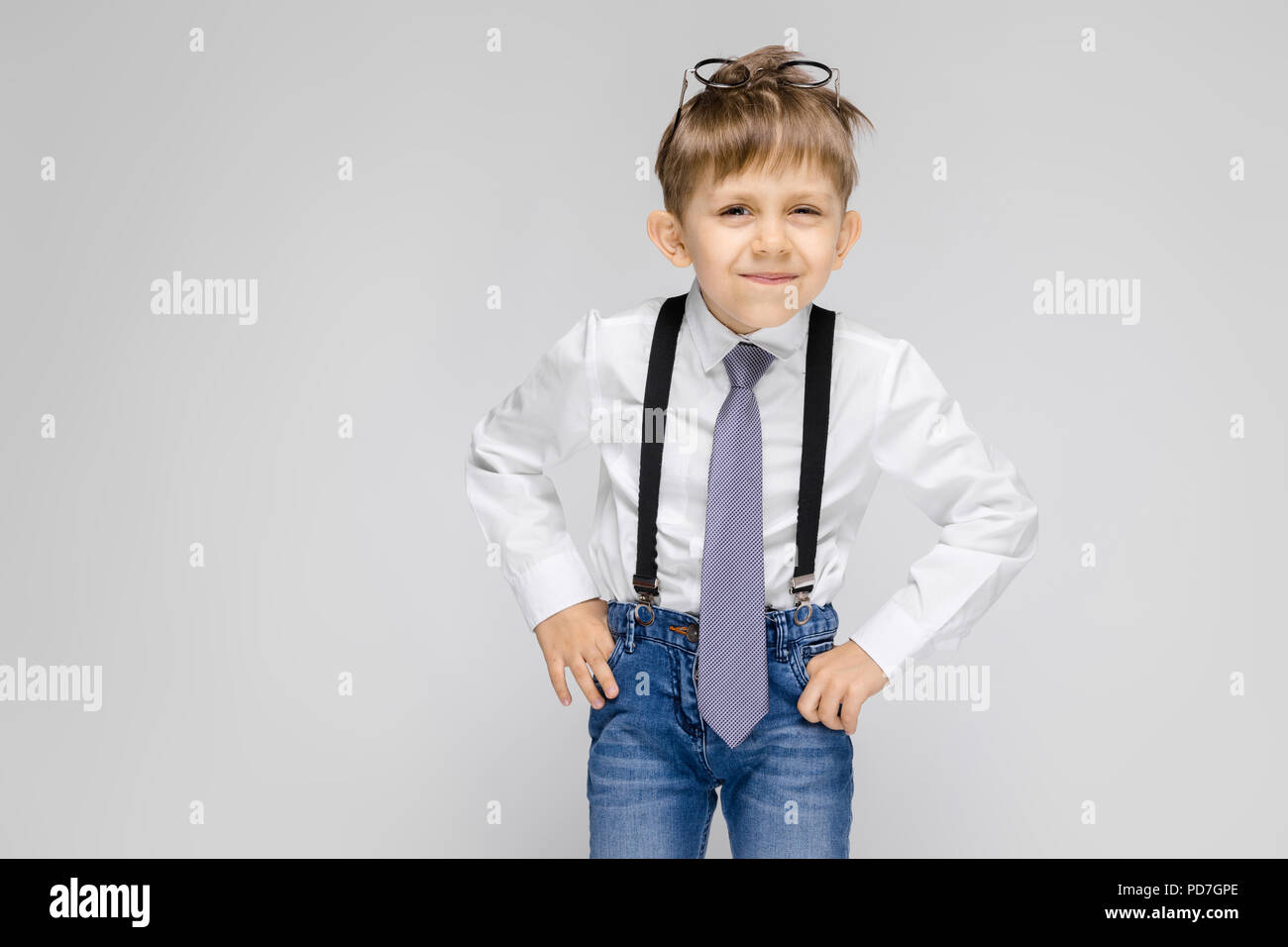 Un charmant garçon dans une chemise blanche, bretelles, une cravate et des  jeans se dresse sur un fond gris. Verres sur la tête Photo Stock - Alamy