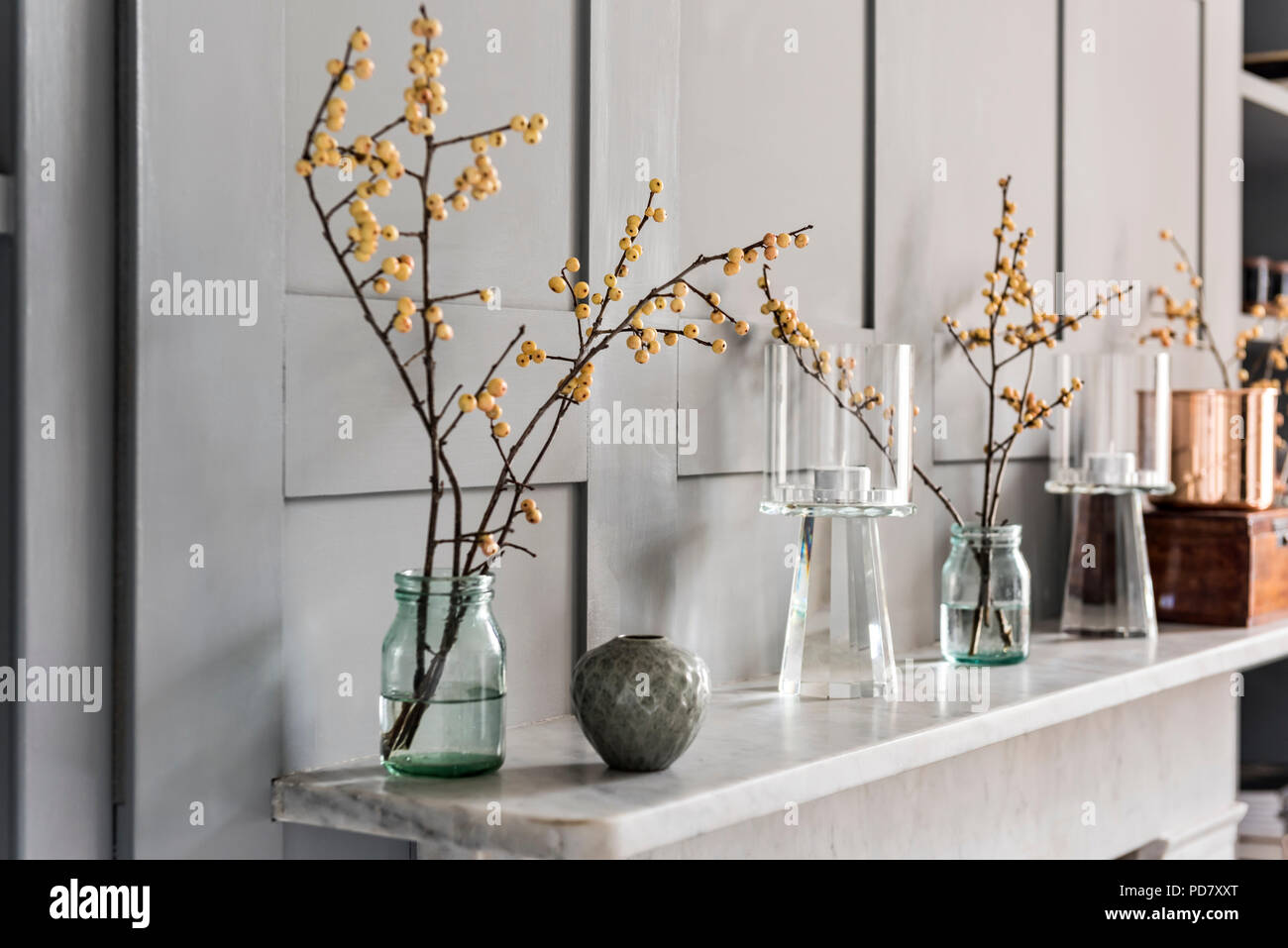 Branches de l'hiver de l'or dans la bouteille de lait en verre et un pot par Akiko Hirai sur la cheminée. Banque D'Images