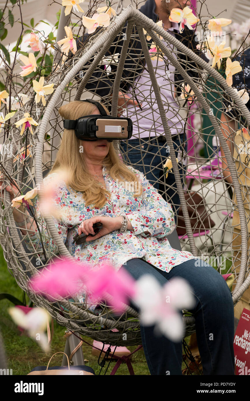 Femme portant un casque VR, assis dans le siège parmi les fleurs à l'expérience de réalité virtuelle orchid - RHS Flower Show de Chatsworth, Derbyshire, Angleterre, Royaume-Uni. Banque D'Images