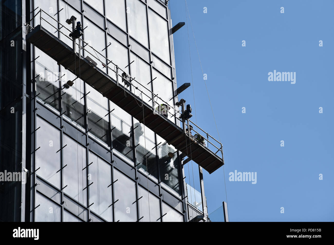 Travailleurs de la construction sur une plate-forme suspendue sur un gratte-ciel à la façade de verre Banque D'Images