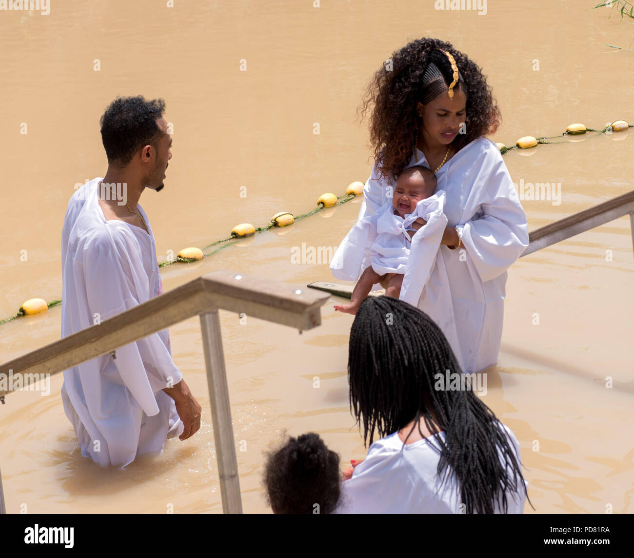Jourdain, Israël 19 mai 2018 pèlerinage chrétien Éthiopien : famille avec un bébé, habillé en blanc, en se faisant baptiser au même endroit du brown Banque D'Images