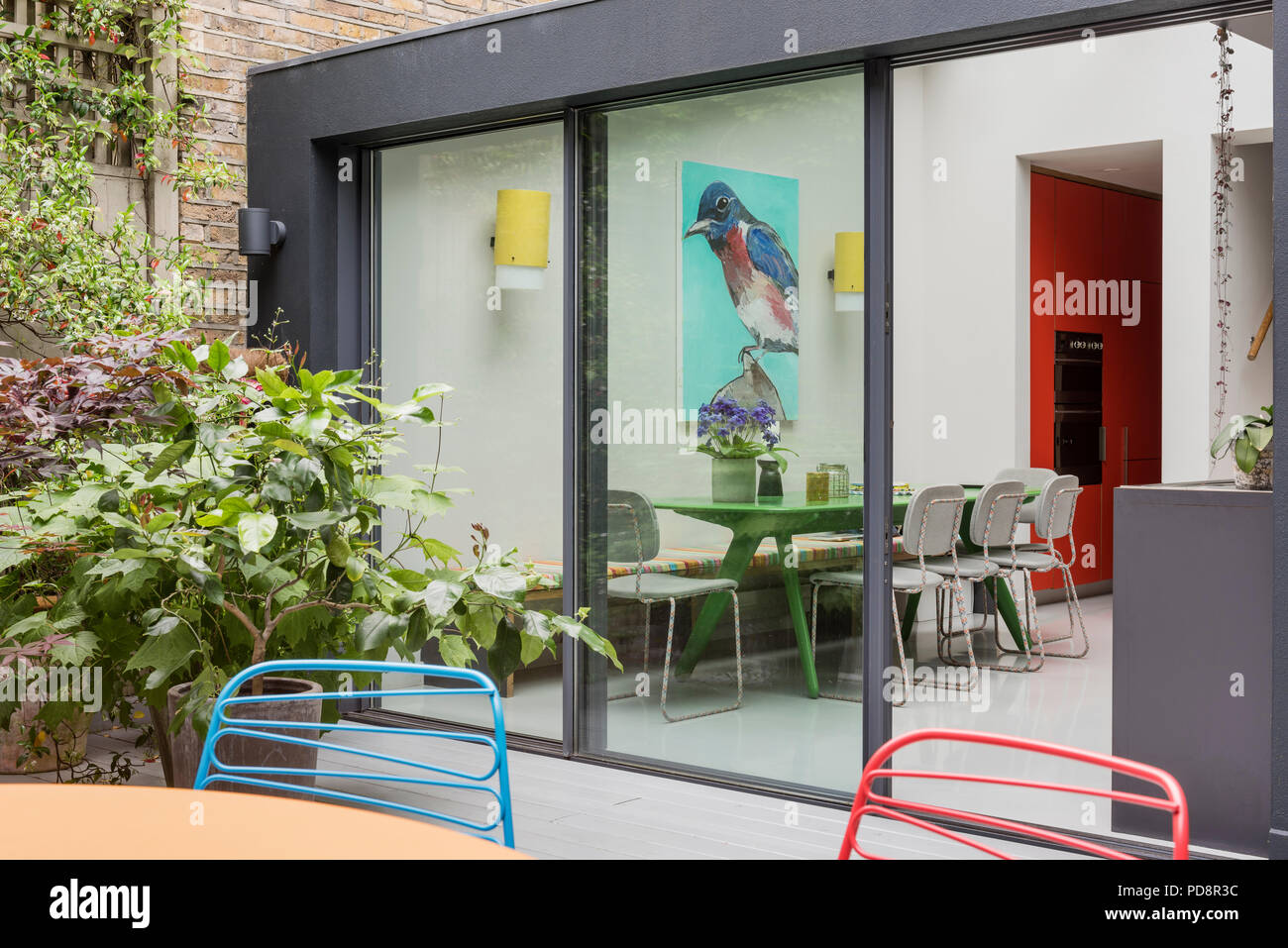 Voir à partir de la terrasse du jardin à la cuisine et d'oiseau portrait par James Franco sur le tableau peint en vert personnalisé par Tom Dixon et chaises de Moooi. Banque D'Images