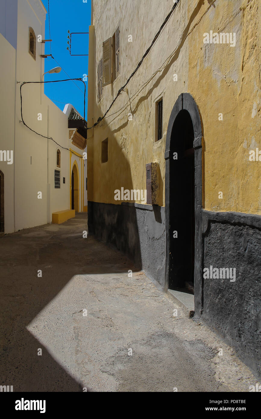 Rue étroite dans l'ancienne forteresse portugaise. Façade d'une maison jaune sur le côté de l'homme. Portes traditionnelles avec les archs. Ciel bleu. El Jadida, Mo Banque D'Images