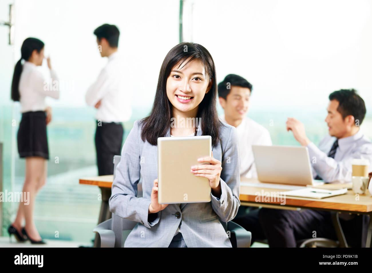 Portrait of young asian business woman holding digital tablet looking at camera smiling in office. Banque D'Images