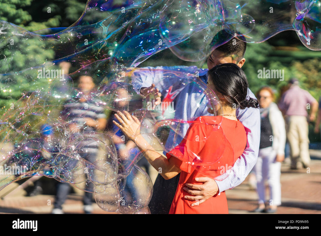 Couple jouant avec des bulles de savon arc-en-ciel géant flottant dans l'air d'été au cours d'une belle journée ensoleillée. Fun jeu amusant pour les enfants et les adultes. Banque D'Images