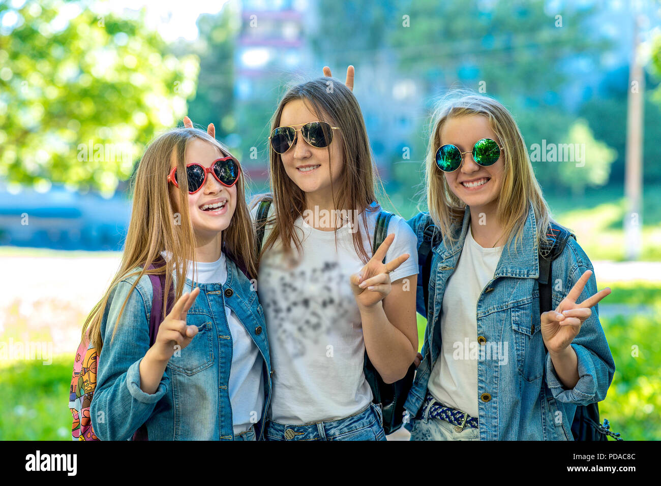 Trois filles adolescente écolière portant des jeans, vêtements et lunettes de soleil. Happy smiling avec geste de mains montrant Bonjour. Les émotions de bonheur et de détente. Le concept est meilleur amis d'école. Banque D'Images