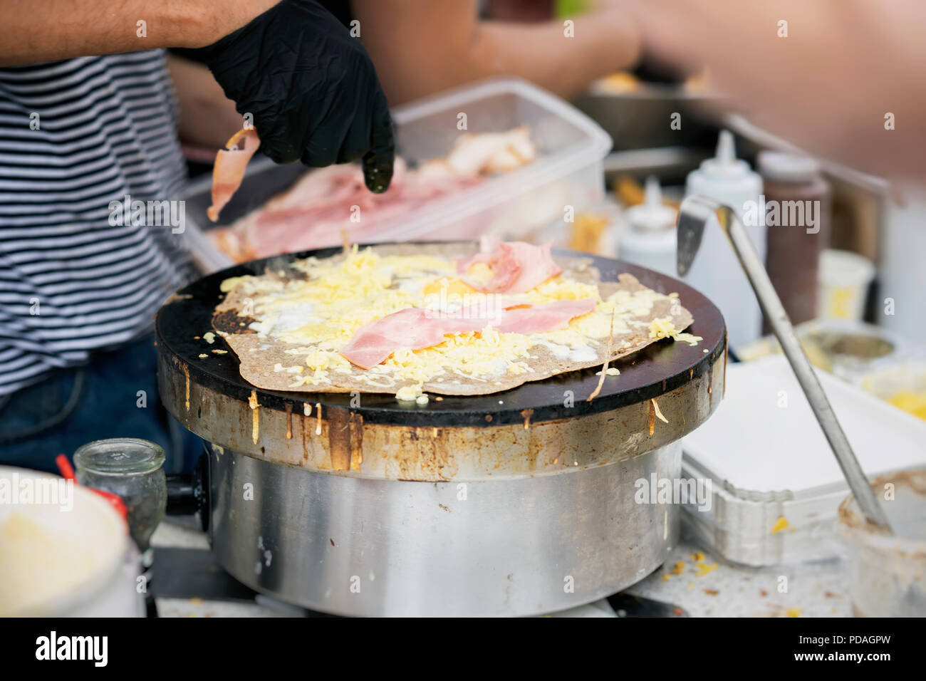 La préparation de crêpe, galette au jambon, fromage et d'oeufs sur la plaque noire. Les mains du cuisinier de l'été, parti de la ville. National Food Concept, très savoureuse restauration rapide, summer party Banque D'Images