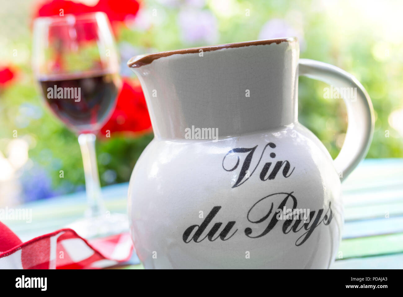 Pichet de vin du pays et un verre de vin rouge pays simples en français sur terrasse avec table de jardin floral derrière dans soleil couchant Banque D'Images