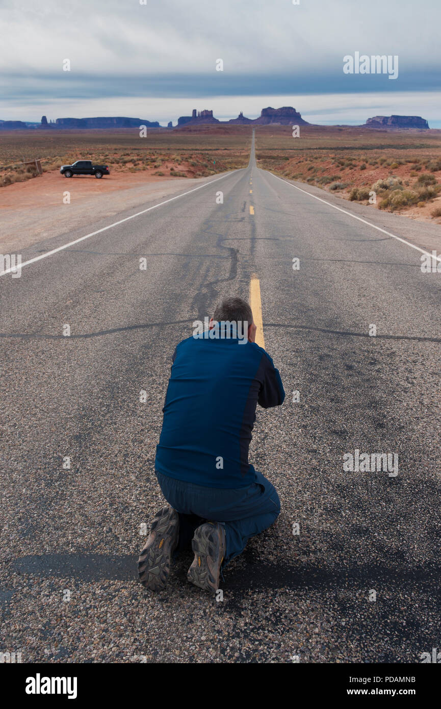 Homme à genoux sur le tarmac pour prendre une photo de la route 163 menant à Monument Valley, Arizona, USA. Banque D'Images