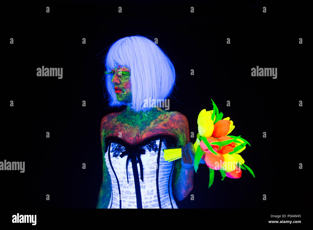 Concept de la séance photo de mariage en éclairage néon style vogue mariée jeune fille brille dans l'obscurité avec hairstyle quads et bouquet posant en robe de mariée blanche sous les rayons UV sur un fond sombre dans le studio Banque D'Images